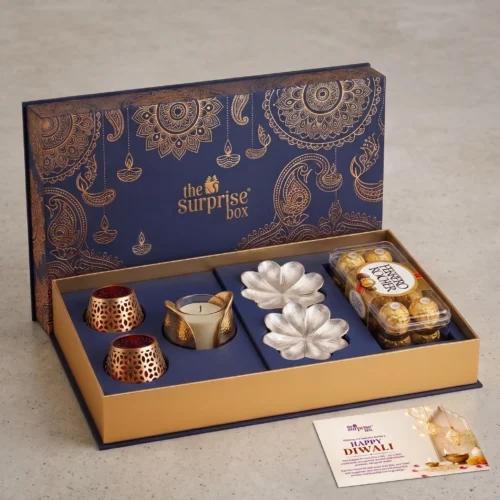 3. The Gift Studio Premium Premium Luxury Hamper Gift set in blue and gold with ornate patterns, containing candles, metal flower molds, and a tray of chocolates from The Surprise Box for Diwali fun.