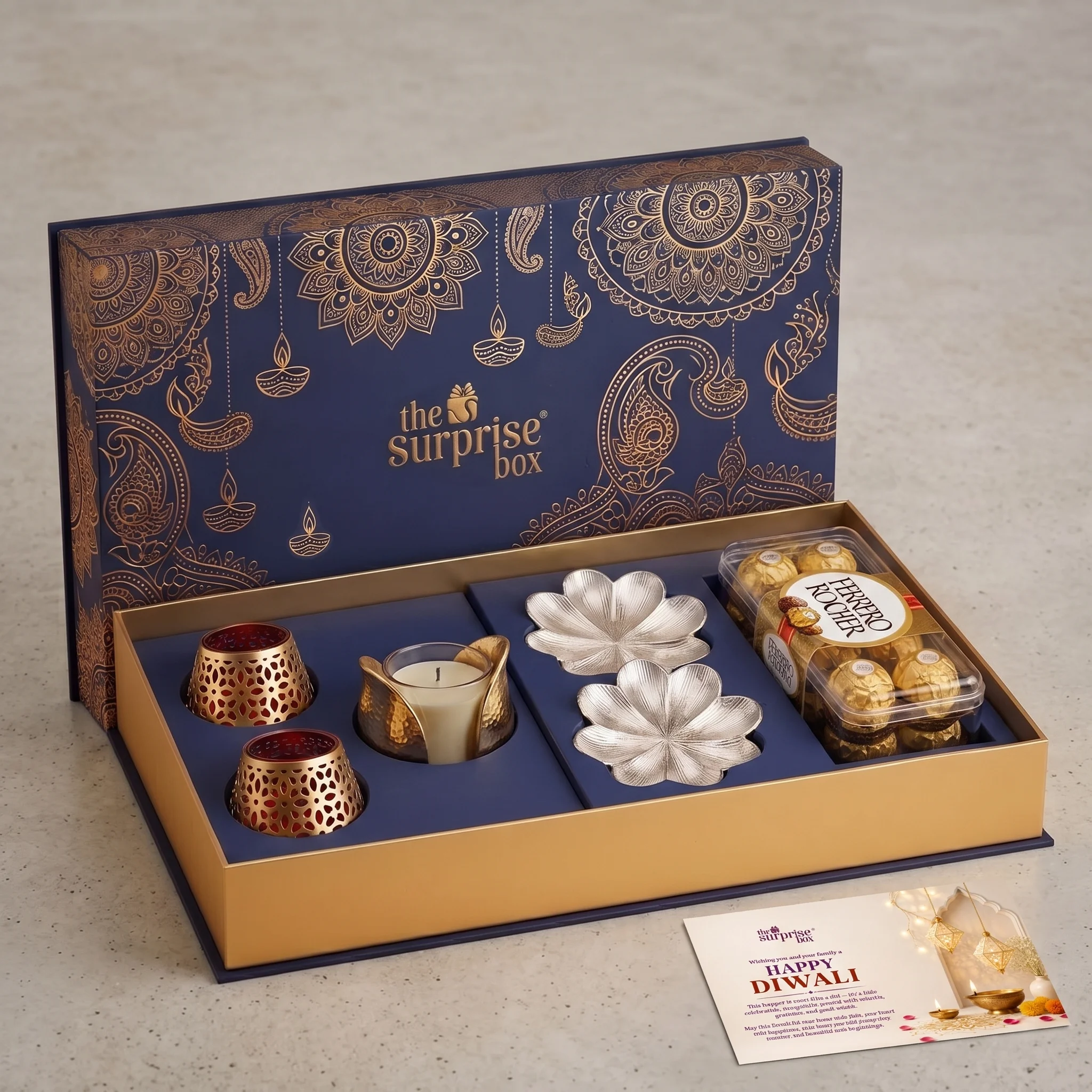 Gift set in blue and gold with ornate patterns, containing candles, metal flower molds, and a tray of chocolates from The Surprise Box for Diwali fun.